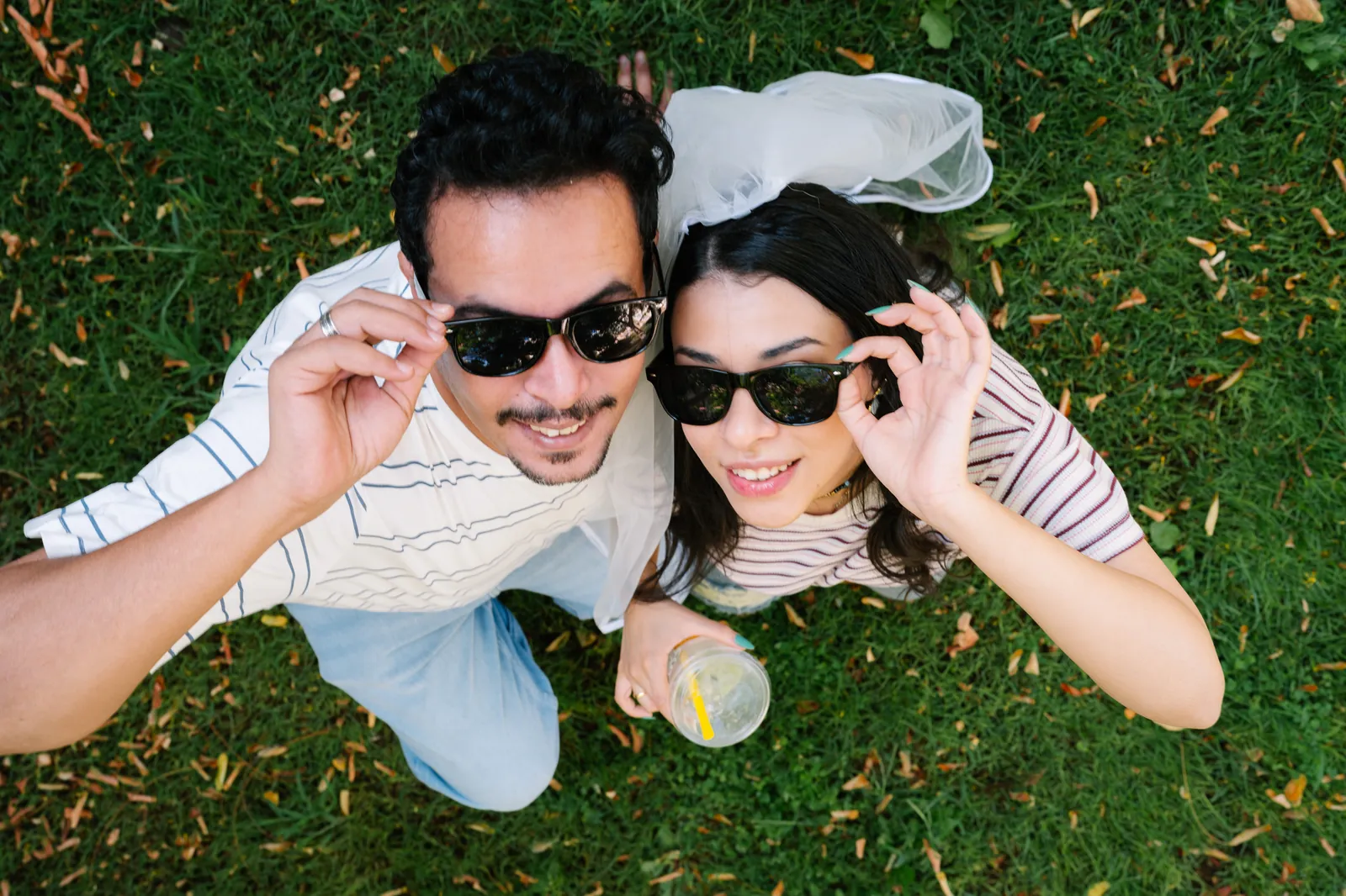 Islam and Nada lying on the grass, smiling up at the camera in matching sunglasses